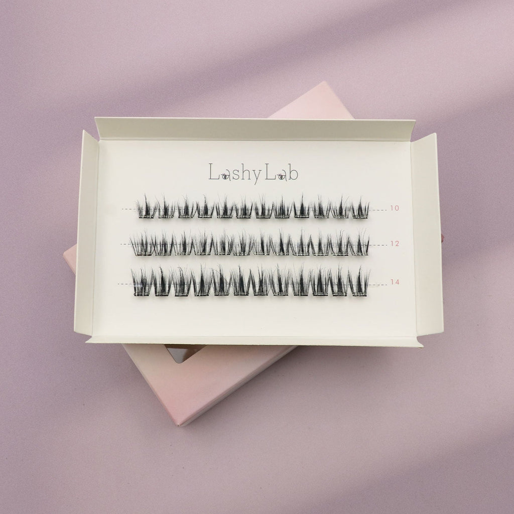 A white box labeled Lashy Lab BARE PRE-GLUED LASHES SET holds three rows of pre-glued cluster lashes in assorted lengths, displayed on a pastel lilac and pink background for easy application.