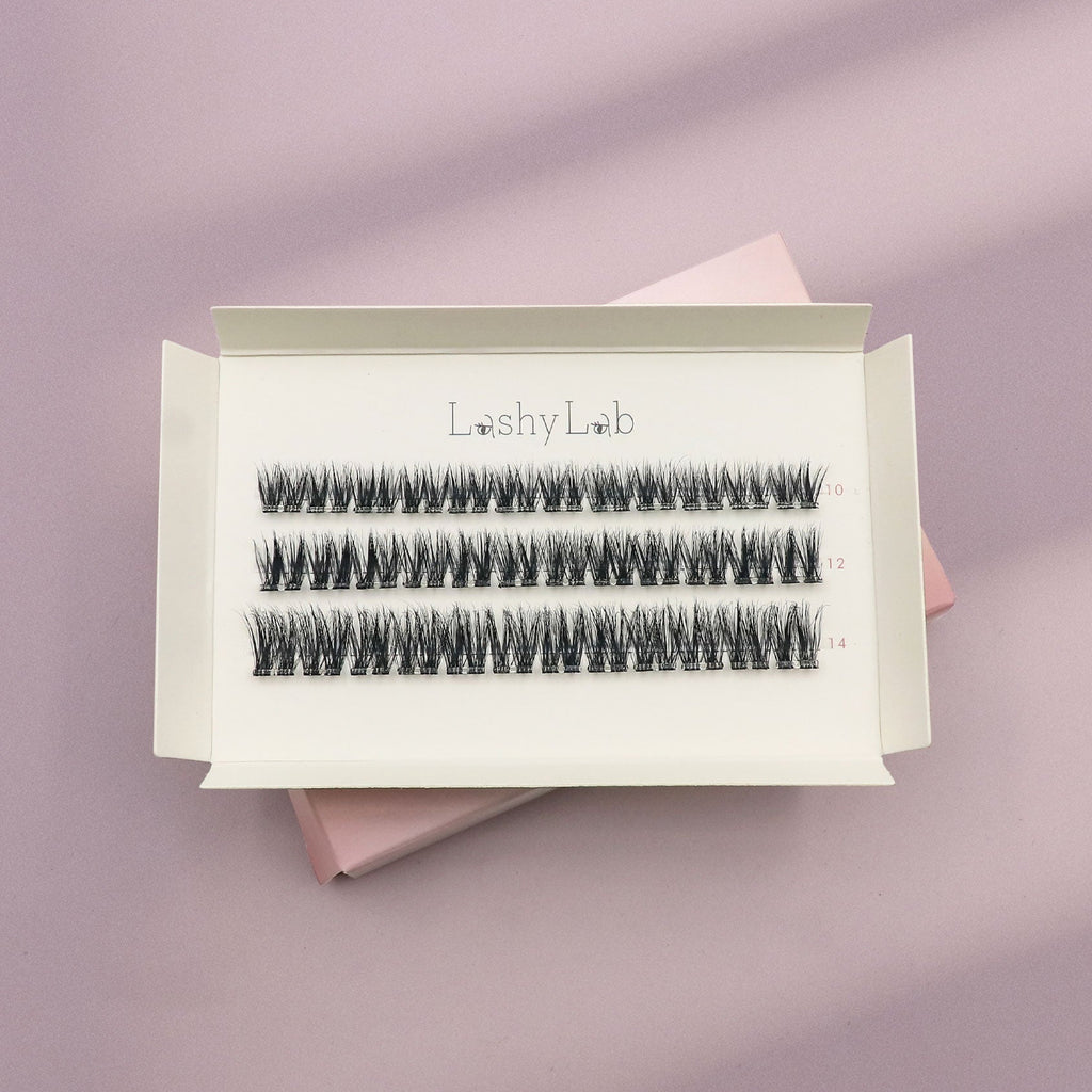 An open box of Lashy Labs FLUTTER Wispy, Voluminous, Full lash extensions rests on a pink surface, showcasing four rows of DIY lashes in 8mm, 10mm and 12mm lengths that stay on for 5-7 days.