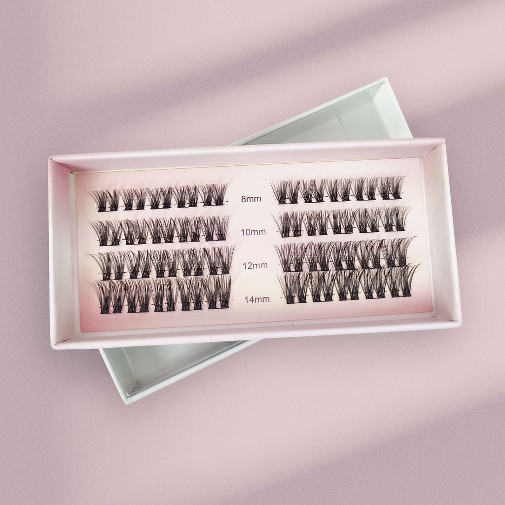 Lashy Labs NIGHT OUT cluster lashes in four rows (8mm, 10mm, 12mm, 14mm) are displayed on a pink surface—full, voluminous, and sassy for DIY eyelash extensions that last weeks.