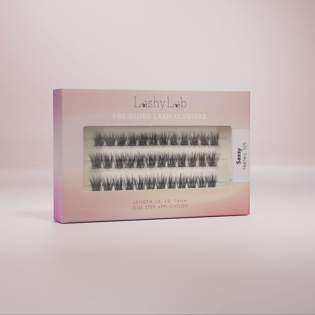 Lashy Lab’s SASSY set features pre-glued lashes in four lengths—8mm, 10mm and 12mm—for effortless, natural beauty. The lashes are arranged in rows and displayed against a pink background.