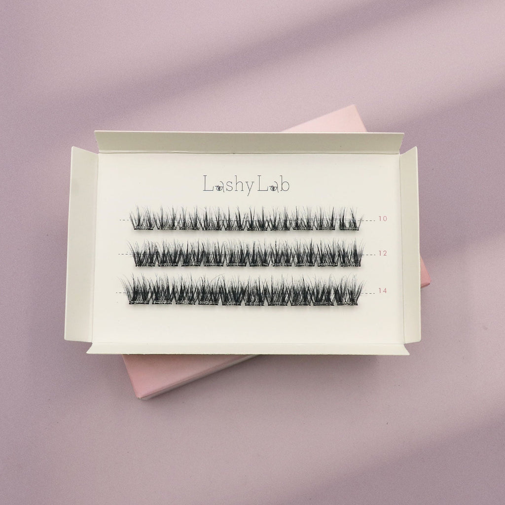 A white box labeled Lashy Lab SIREN PRE-GLUED LASHES SET holds three rows of pre-glued cluster lashes in assorted lengths, displayed on a pastel lilac and pink background for easy application.